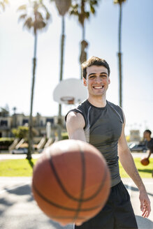 Lächelnder junger Mann hält Basketball auf einem Platz im Freien - LEF000103