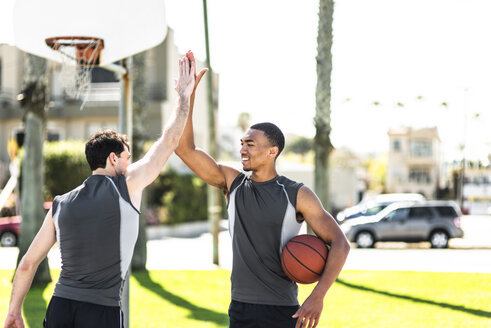 Zwei junge Männer, die sich auf einem Basketballplatz im Freien die Hände reichen - LEF000113