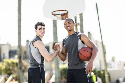 Zwei junge Männer schütteln sich auf einem Basketballplatz im Freien die Hände - LEF000115