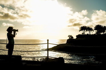 Spanien, Teneriffa, Frau beim Fotografieren am Meer bei Sonnenuntergang - SIPF000361