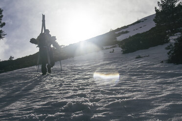 Gegenlicht eines Mannes mit Skiern im Rucksack, der im Schnee im Peñalara-Gebirge, Madrid, Spanien, läuft - ABZF000355