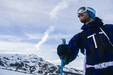 Man with ski goggles holding a ski pole in a snowy mountain landscape - ABZF000362