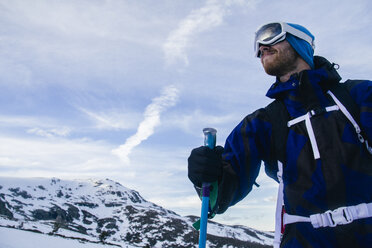 Mann mit Skibrille hält einen Skistock in einer verschneiten Berglandschaft - ABZF000362