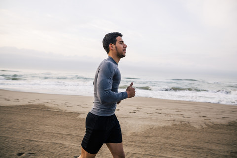Junger Mann läuft am Strand, lizenzfreies Stockfoto