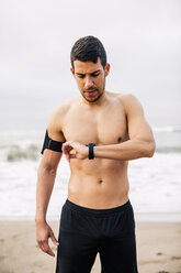 Sportlicher junger Mann am Strand mit Blick auf die Uhr - EBSF001310