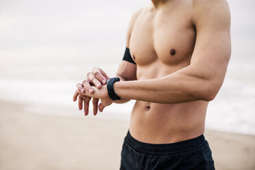 Sportlicher junger Mann am Strand beim Einstellen der Uhr - EBSF001313