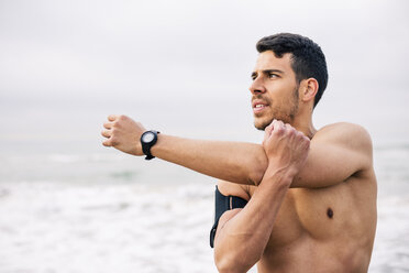 Sportive young man stretching on the beach - EBSF001314