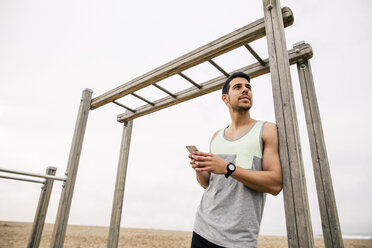 Young man resting at monkey bars on the beach - EBSF001327