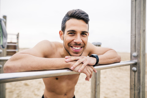 Porträt eines lächelnden Sportlers am Barren am Strand, lizenzfreies Stockfoto