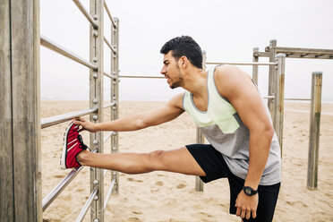 Young man stretching on wall bars on the beach - EBSF001340