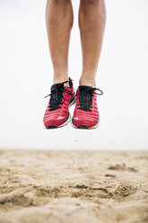 Legs of athlete jumping mid-air in sand - EBSF001345