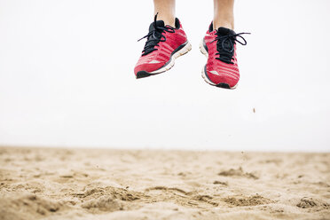 Legs of athlete jumping mid-air in sand - EBSF001346