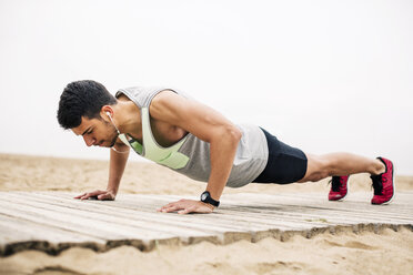 Young man doing push-ups on boardwalk on the beach - EBSF001348