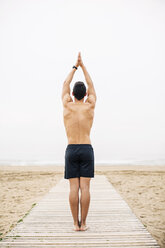 Junger Mann übt Yoga auf der Strandpromenade am Strand - EBSF001352