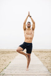 Junger Mann übt Yoga auf der Strandpromenade am Strand - EBSF001353