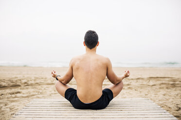 Young man practicing yoga on boardwalk on the beach - EBSF001354