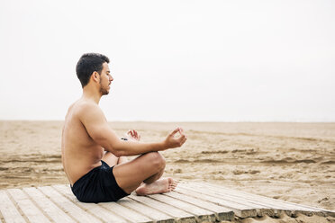 Young man practicing yoga on boardwalk on the beach - EBSF001355