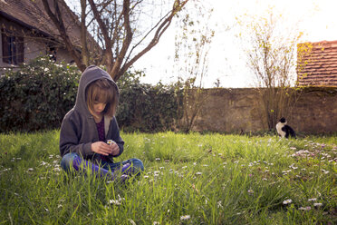 Girl wearing hooded jacket sitting on flower meadow - LVF004777