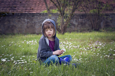 Girl wearing hooded jacket sitting on flower meadow - LVF004778