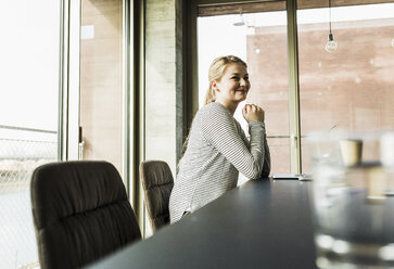 Lächelnde junge Frau am Schreibtisch im Büro - UUF006964