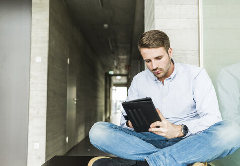 Junger Mann sitzt auf dem Boden und benutzt ein digitales Tablet - UUF006976