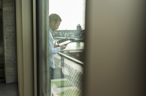 Junger Mann auf Balkon mit digitalem Tablet, lizenzfreies Stockfoto