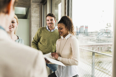 Three smiling colleagues in office looking at mature woman - UUF006990