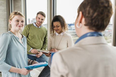 Drei lächelnde Kollegen im Büro betrachten eine reife Frau, lizenzfreies Stockfoto