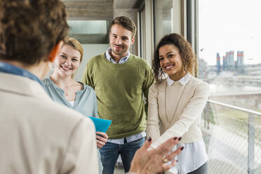 Three smiling colleagues in office looking at talking mature woman - UUF006993