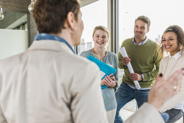 Three happy colleagues in office looking at talking mature woman - UUF006994