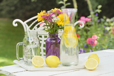 Aufgegossenes Zitronenwasser und frische Zitronen auf dem Gartentisch - ECF001879