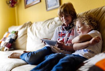 Two boys sitting on couch using digital tablet - MGOF001739