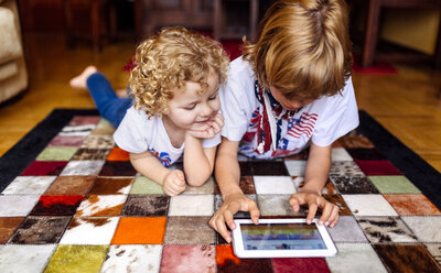 Zwei Jungen liegen zu Hause auf dem Boden und spielen mit einem digitalen Tablet - MGOF001743