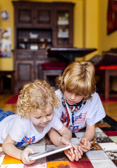 Two boys lying on the floor at home playing with digital tablet - MGOF001746