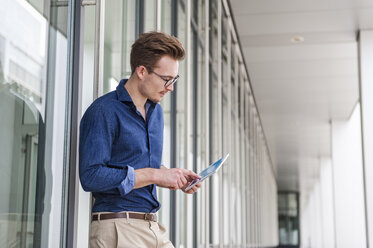 Junger Geschäftsmann steht vor einem Bürogebäude und benutzt ein digitales Tablet - DIGF000311