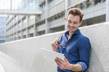 Porträt eines jungen Geschäftsmannes, der an der Wand lehnt und auf ein digitales Tablet schaut - DIGF000318