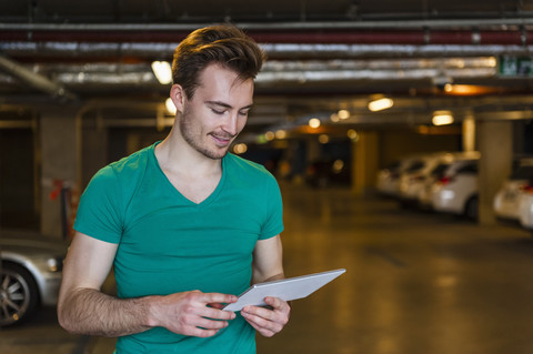 Porträt eines lächelnden jungen Mannes mit digitalem Tablet in einer Tiefgarage, lizenzfreies Stockfoto