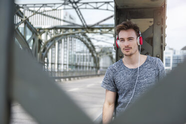 Porträt eines jungen Mannes auf einer Brücke, der mit Kopfhörern Musik hört - DIGF000335