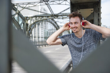 Portrait of smiling young man on a bridge listening with headphones - DIGF000336