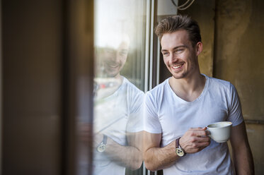 Porträt eines jungen Mannes mit einer Tasse Kaffee, der durch das Fenster schaut - DIGF000344