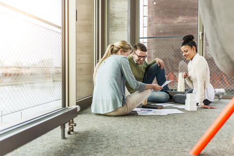 Drei Kollegen im Büro sitzen auf dem Boden und arbeiten zusammen, lizenzfreies Stockfoto