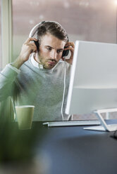 Man at office desk wearing headphones - UUF007022