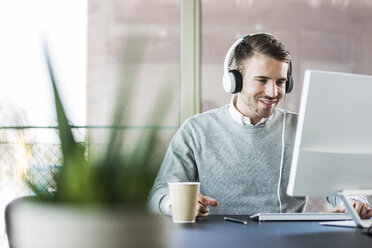 Man at office desk wearing headphones - UUF007024