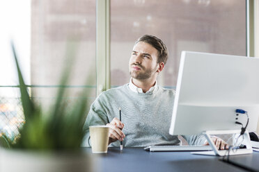 Young man at office desk thinking - UUF007025