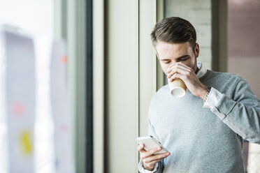 Junger Mann mit Kaffee zum Mitnehmen schaut auf sein Handy - UUF007029