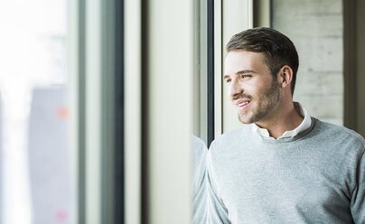 Lächelnder junger Mann schaut aus dem Fenster - UUF007031