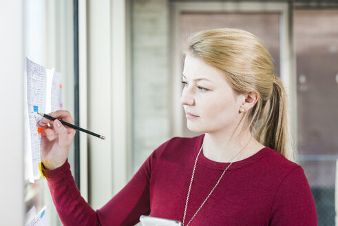 Junge Frau schaut schreibend auf Papier am Fenster - UUF007047