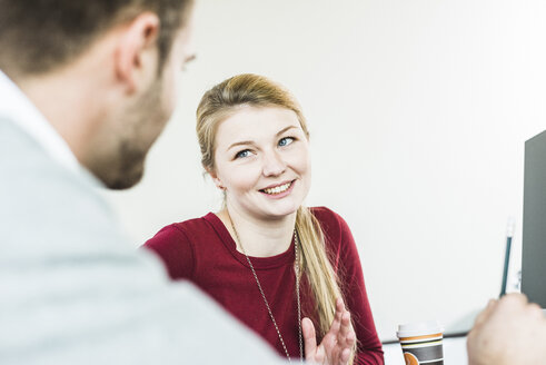 Lächelnde junge Frau schaut einen Kollegen im Büro an - UUF007056