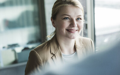 Lächelnde junge Frau im Büro mit Blick auf einen Kollegen - UUF007066