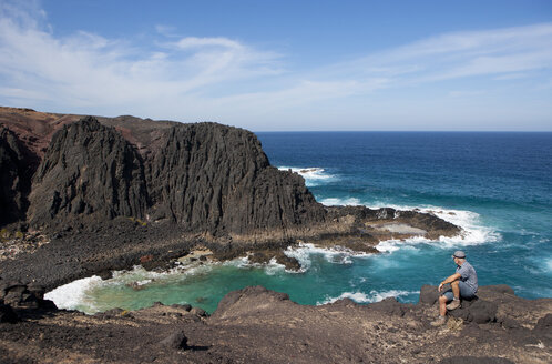 Spain, Canary Islands, Fuerteventura, Punta del mal Rayo, Agua Cabras, hiker sitting on stone - WWF003963